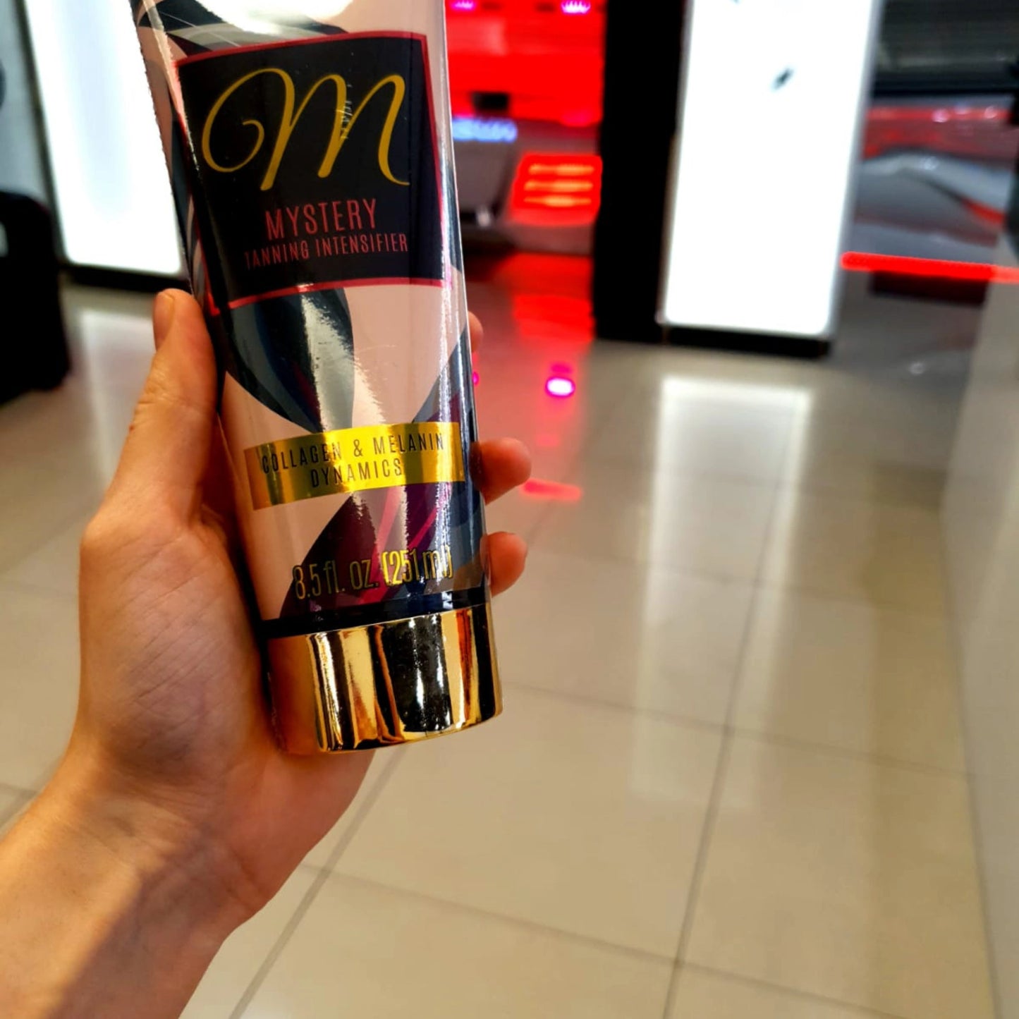 La Loción Bronceadora Onyx Mystery presentada en la mano dentro de un salón profesional con luz roja