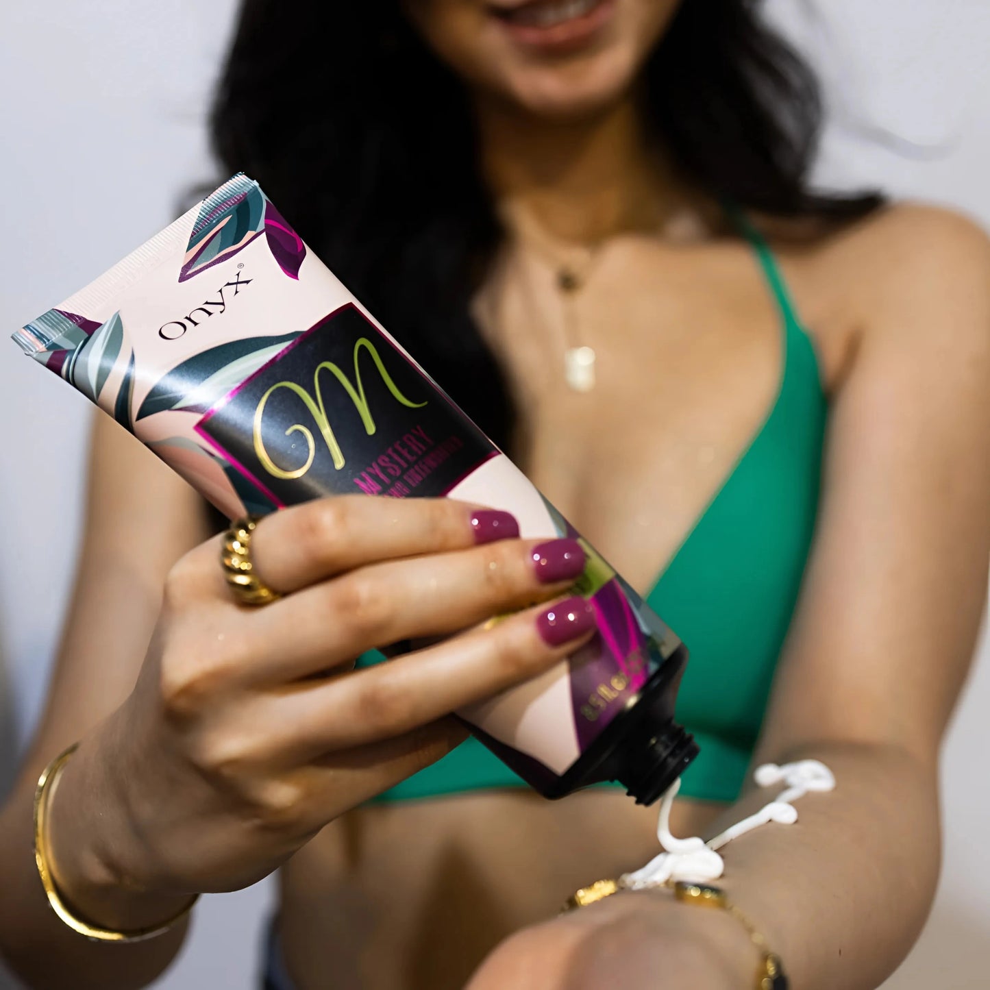 Primer plano de una mujer en bikini verde aplicando la Loción Bronceadora Onyx Mystery con la mano