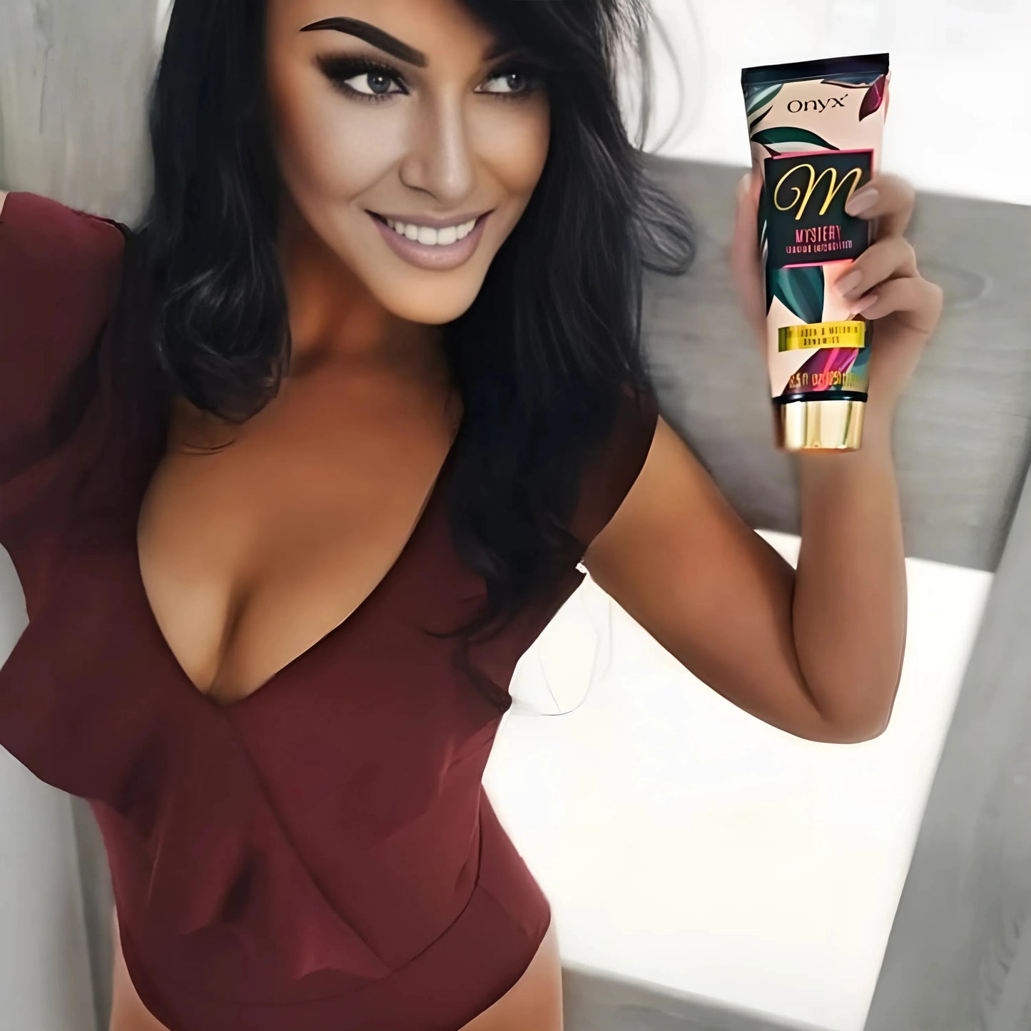 Mujer morena sostiene la Loción Bronceadora Onyx Mystery en la mano y posa con elegante ropa roja