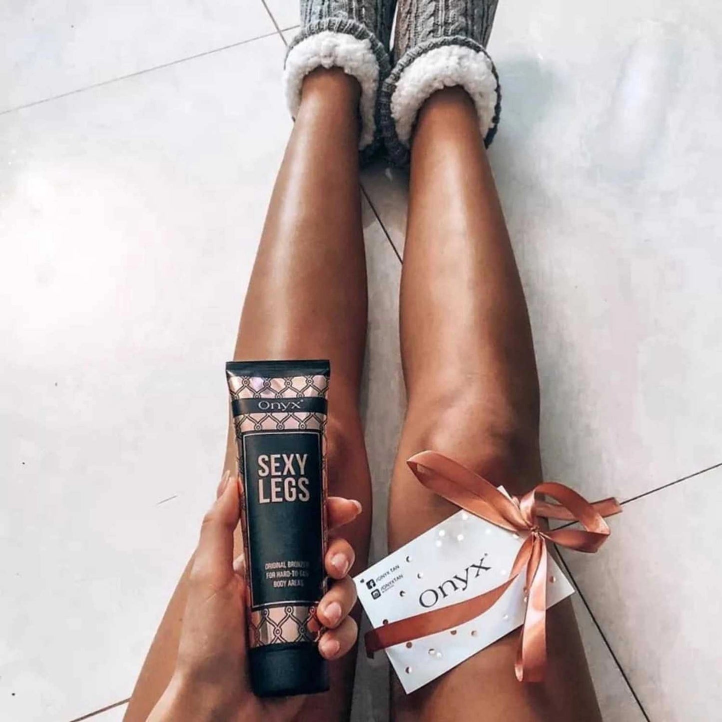Onyx Sexy Legs Lotion junto a unas piernas con lazo de regalo y tarjeta en el suelo