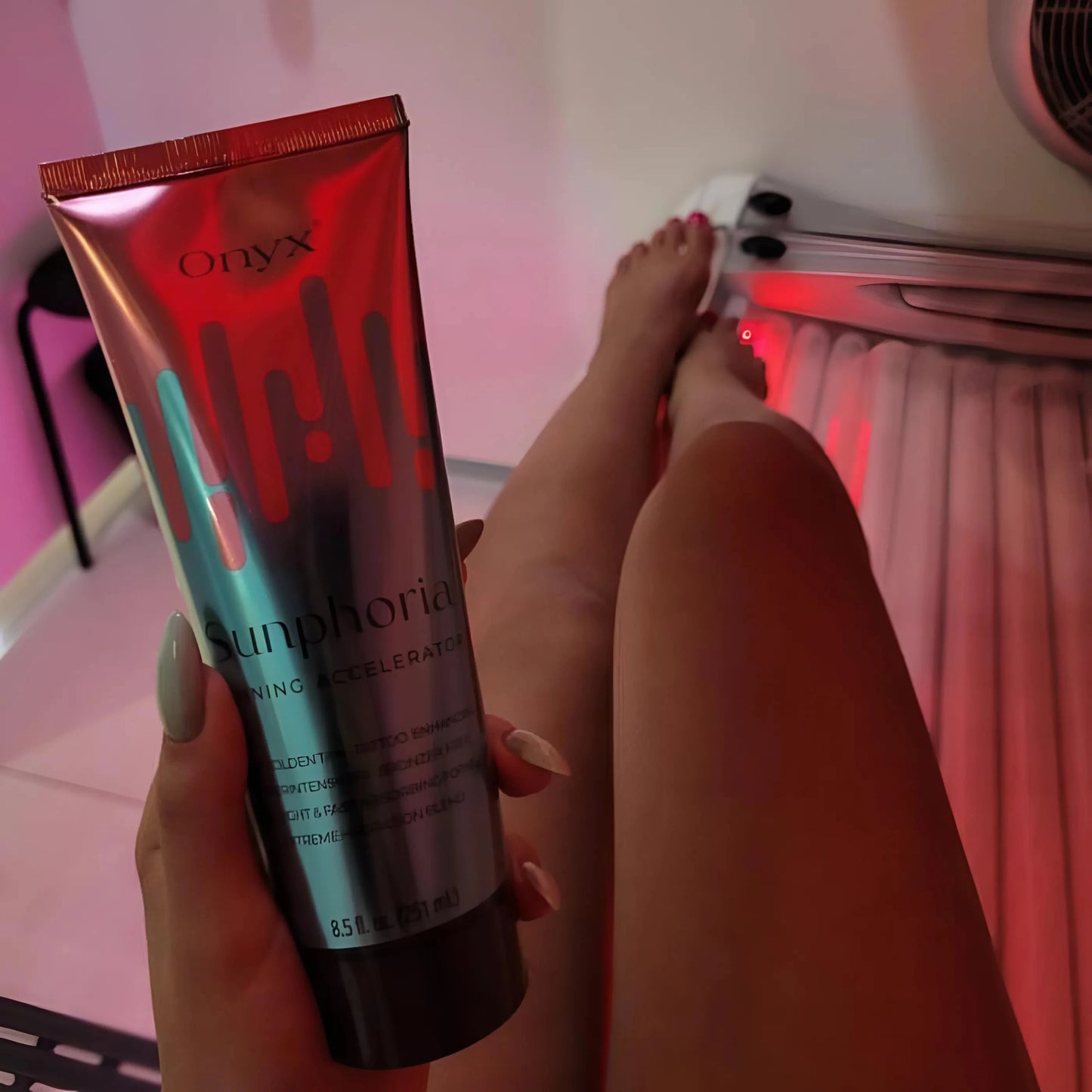 La Loción Bronceadora Onyx Sunphoria sostenida frente a piernas en cama solar