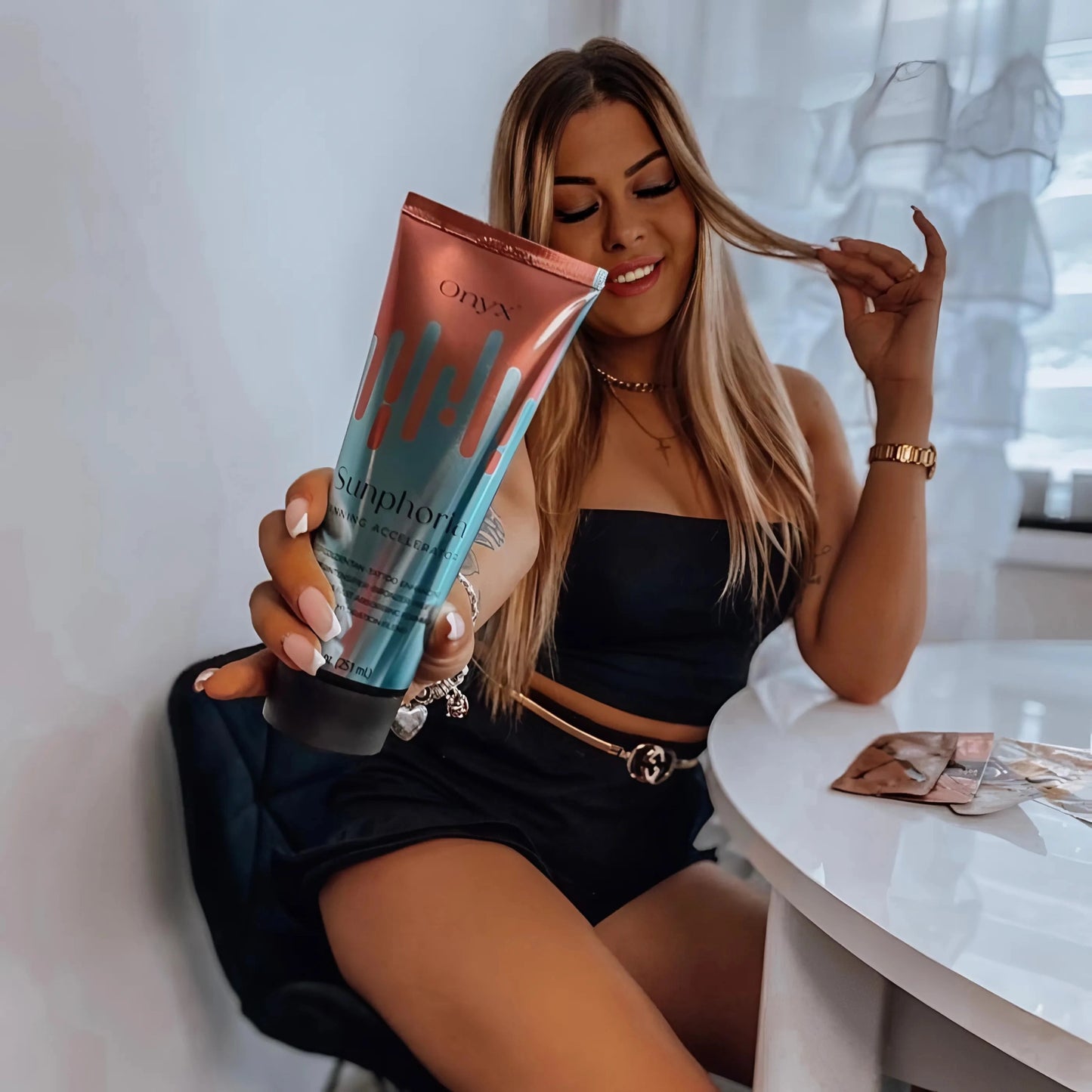 Mujer de cabello largo sostiene la Loción Bronceadora Onyx Sunphoria en la mesa