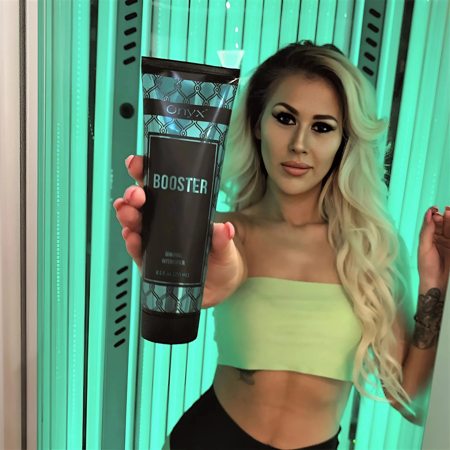 Mujer rubia en el solarium sostiene la Loción Onyx Tanning Booster directamente hacia la cámara – escena ideal de bronceado interior con estilo
