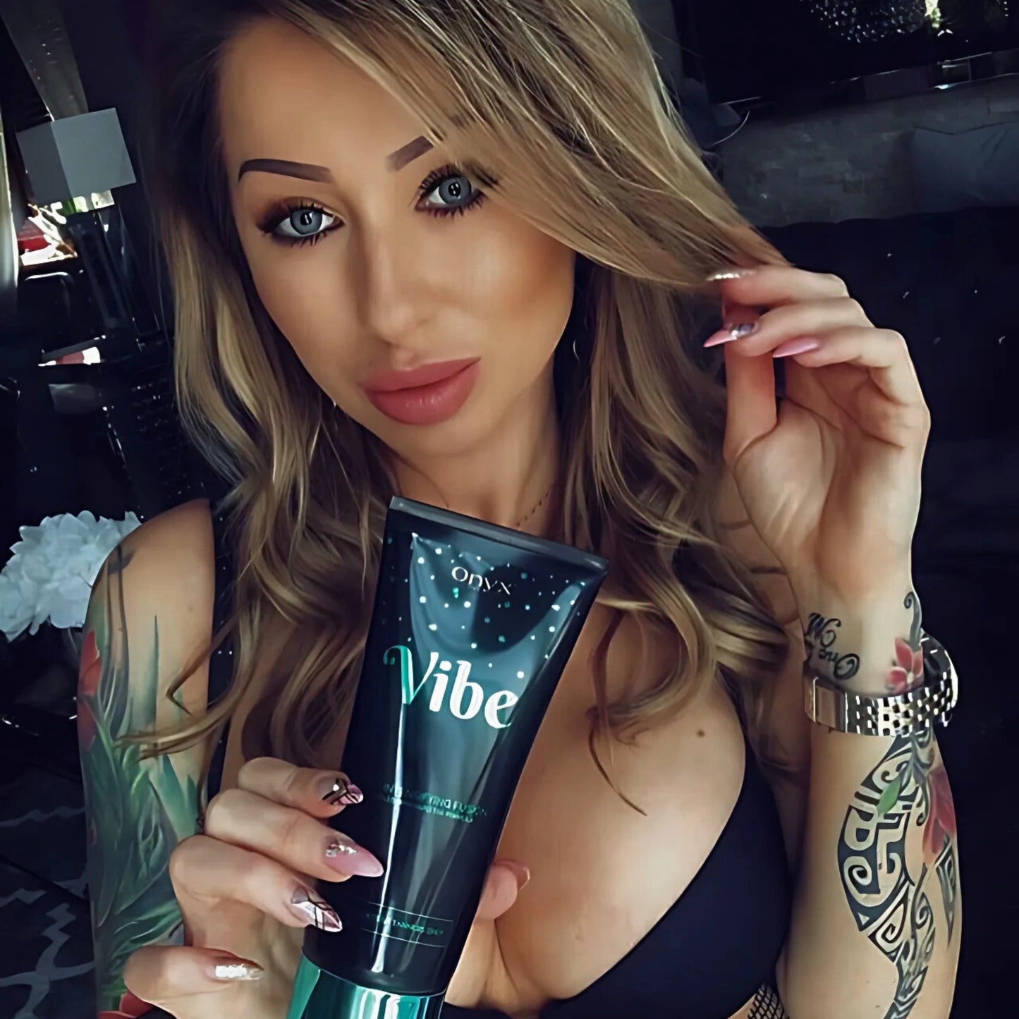Mujer con tatuajes sostiene la Loción Bronceadora Onyx Vibe en la mano – cuidado específico para piel bronceada con estilo individual