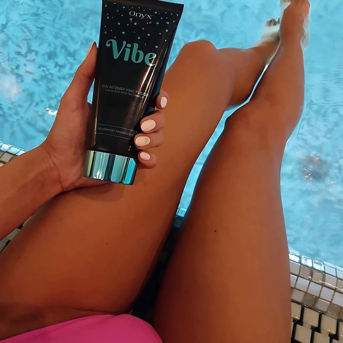 Piernas en el borde de la piscina con la Loción Bronceadora Onyx Vibe en la mano – ambiente relajado con cuidado de bronceado intenso y de acción rápida