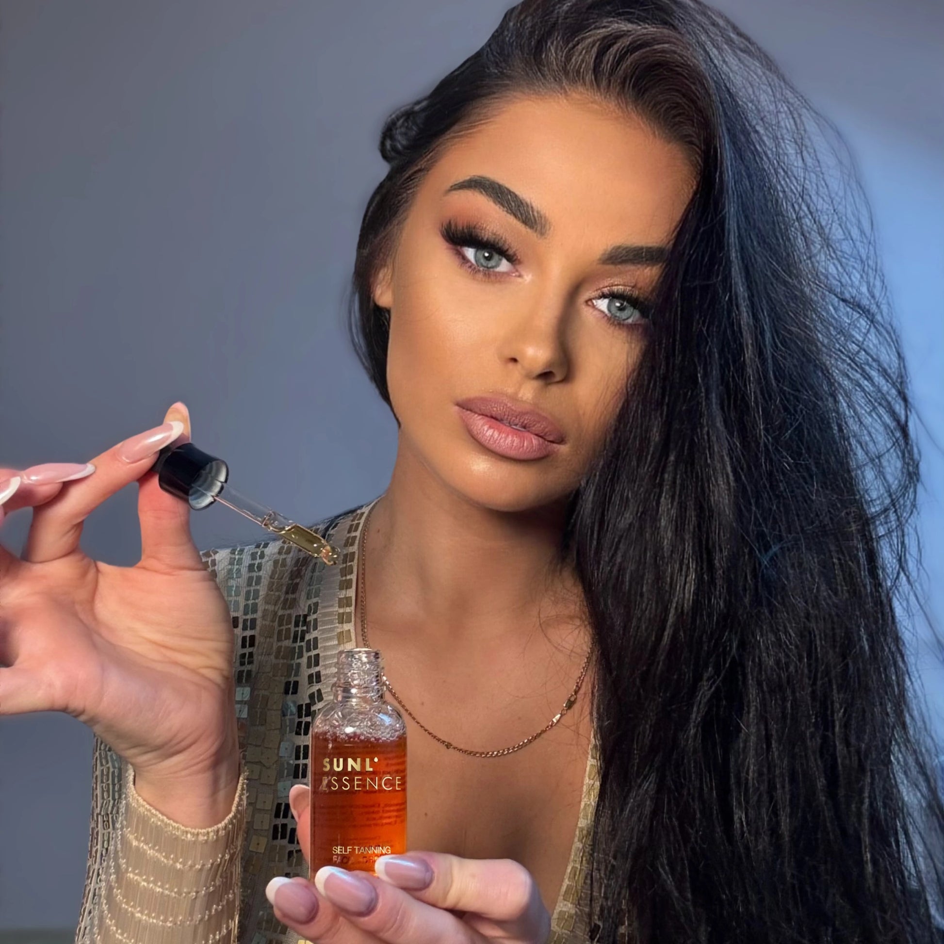 Mujer con vestido dorado sostiene la pipeta de las Gotas Sunl’essence sobre el frasco