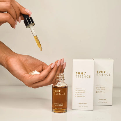 Pipeta de las Gotas Sunl’essence sobre mano con crema, envases al fondo