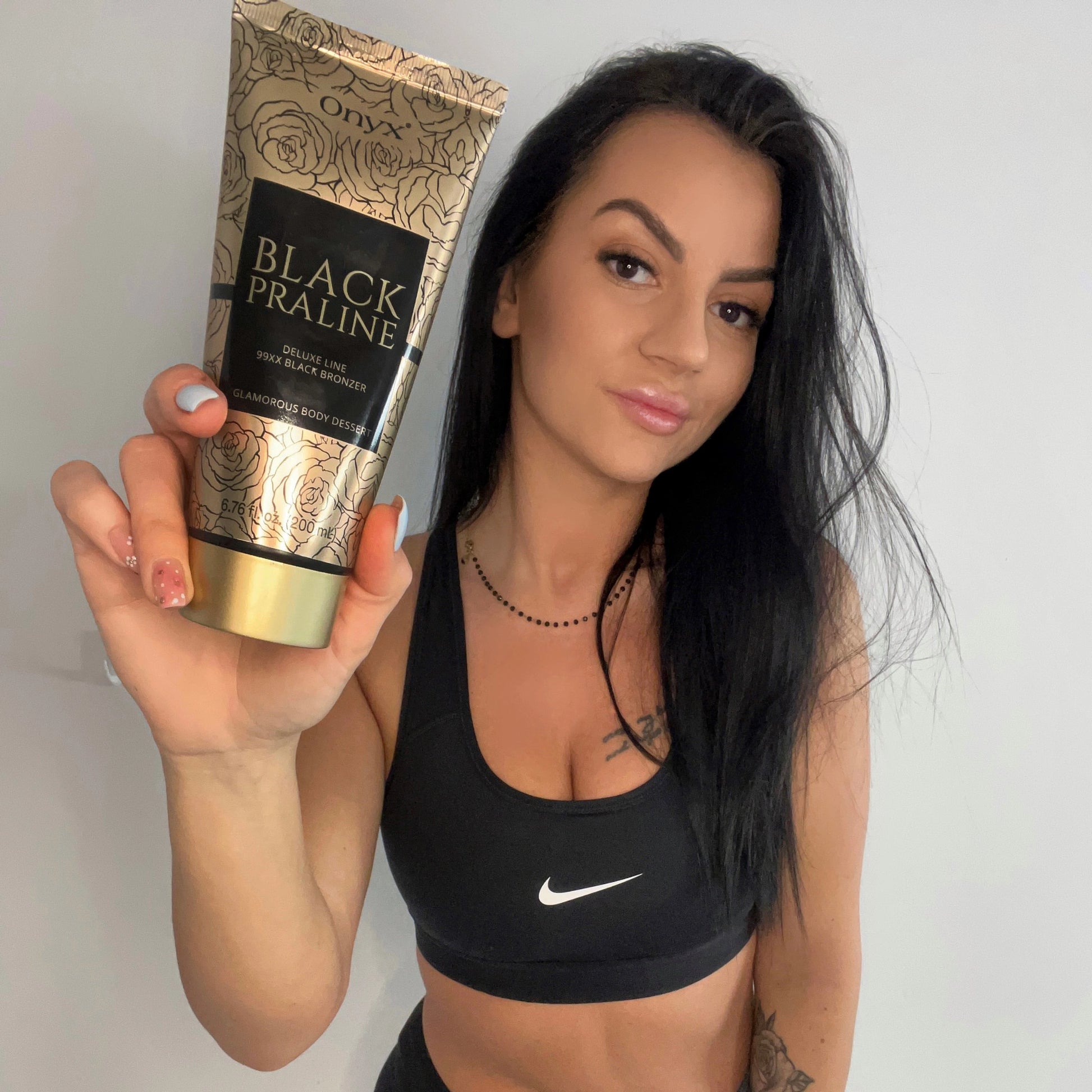 Mujer con top deportivo negro sostiene la loción Onyx Black Praline directamente hacia la cámara