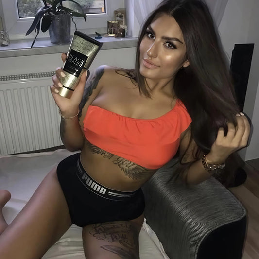 Mujer tatuada con top naranja presenta la loción Onyx Black Praline en la sala de estar