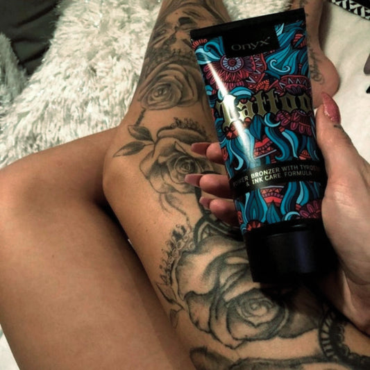 Loción bronceadora Onyx Tattoo sostenida junto a piernas tatuadas, realzando la durabilidad del tatuaje y los efectos de un bronceado intenso.