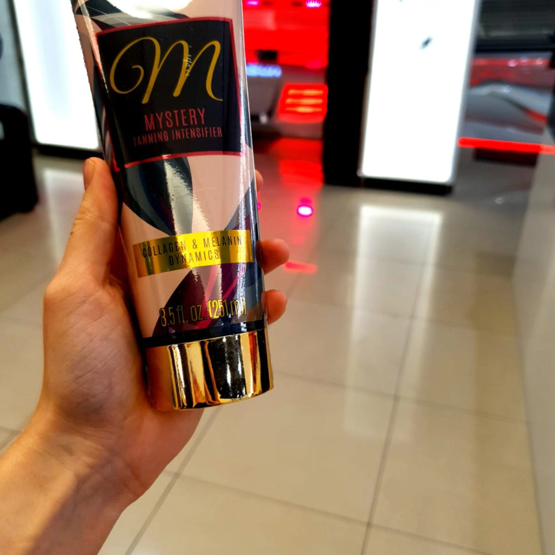 La Loción Bronceadora Onyx Mystery presentada en la mano dentro de un salón profesional con luz roja