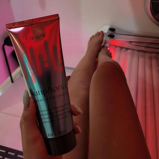 La Loción Bronceadora Onyx Sunphoria sostenida frente a piernas en cama solar