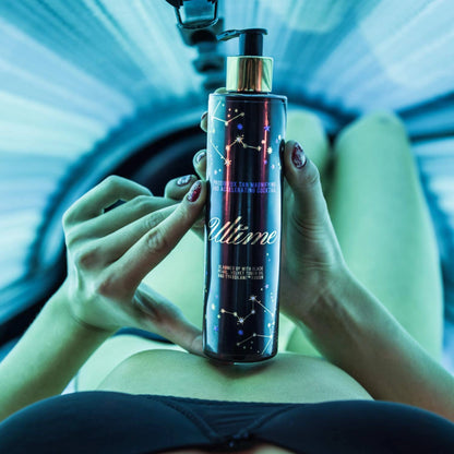 Mujer recostada en el solarium sostiene la Loción Bronceadora Onyx Ultime con ambas manos frente a su abdomen bajo luz azulada